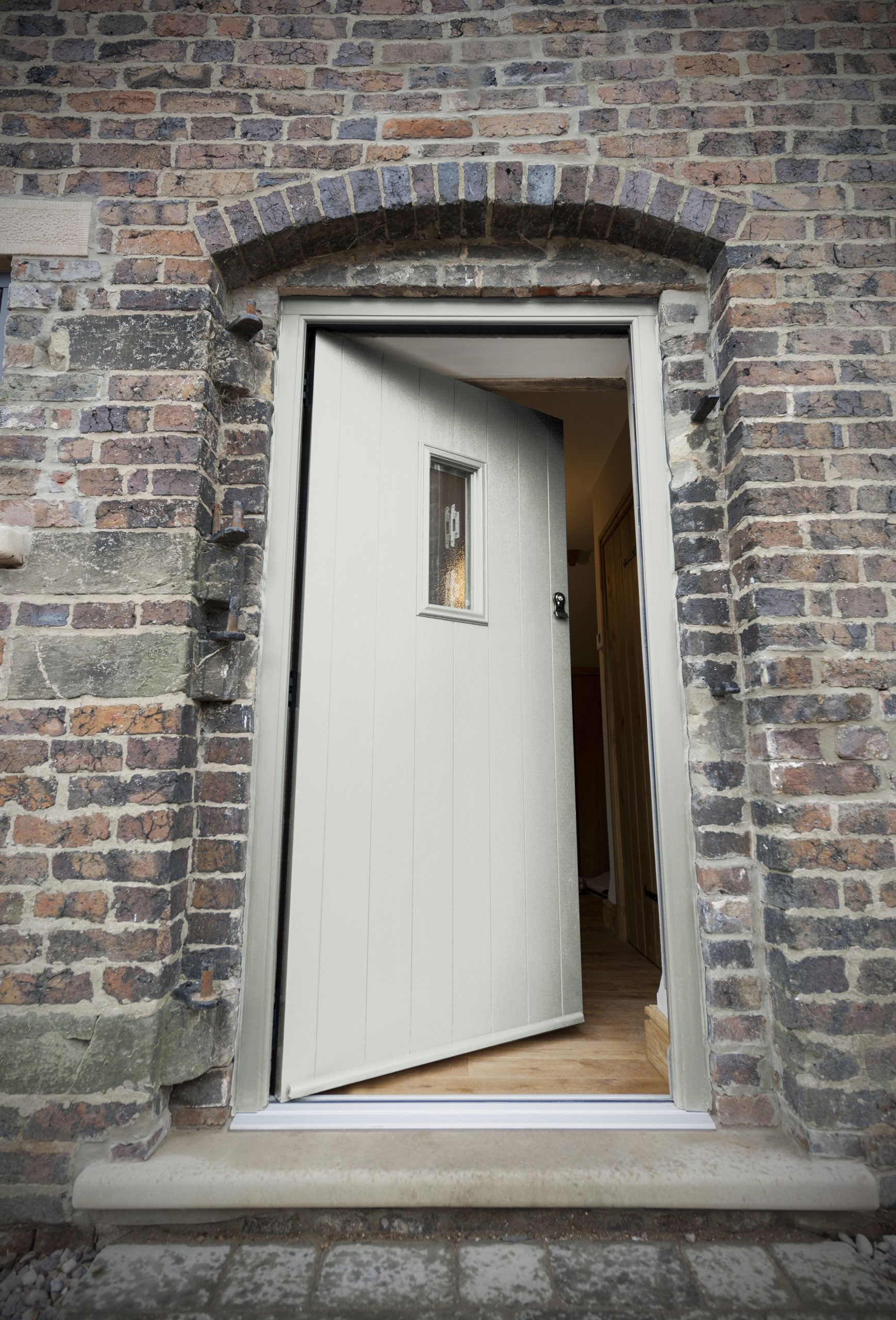 Painswick Grey Solidor composite front door partially open in an arched brick doorway